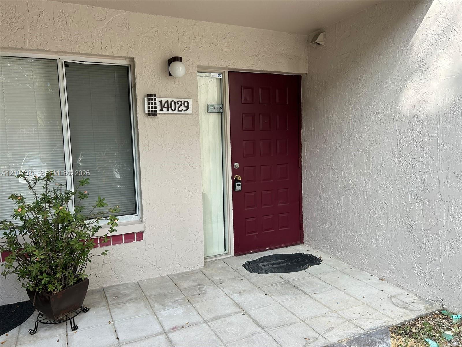 Entryway featuring a solid panel front door, textured exterior stucco, square ceramic tile flooring, and a glass-paneled sidelight