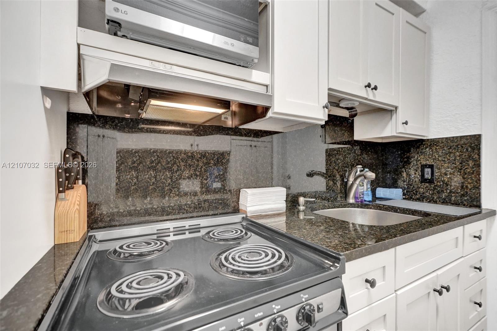 Kitchen featuring white cabinetry, dark stone countertops, integrated backsplash, stainless steel electric range, and an under-mounted sink