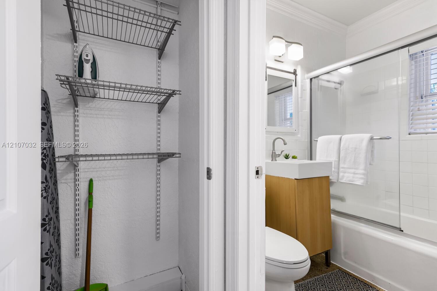 Built-in wire shelving, vanity with vessel sink, wall-mounted faucet, and glass-enclosed shower featuring tiled surround