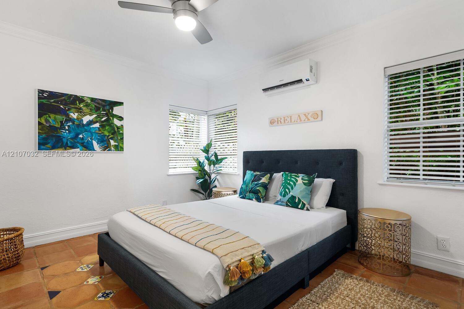 Room featuring terra-cotta tile flooring with decorative inlay accents, multi-pane windows with integrated blinds, ceiling fan, and wall-mounted climate control unit