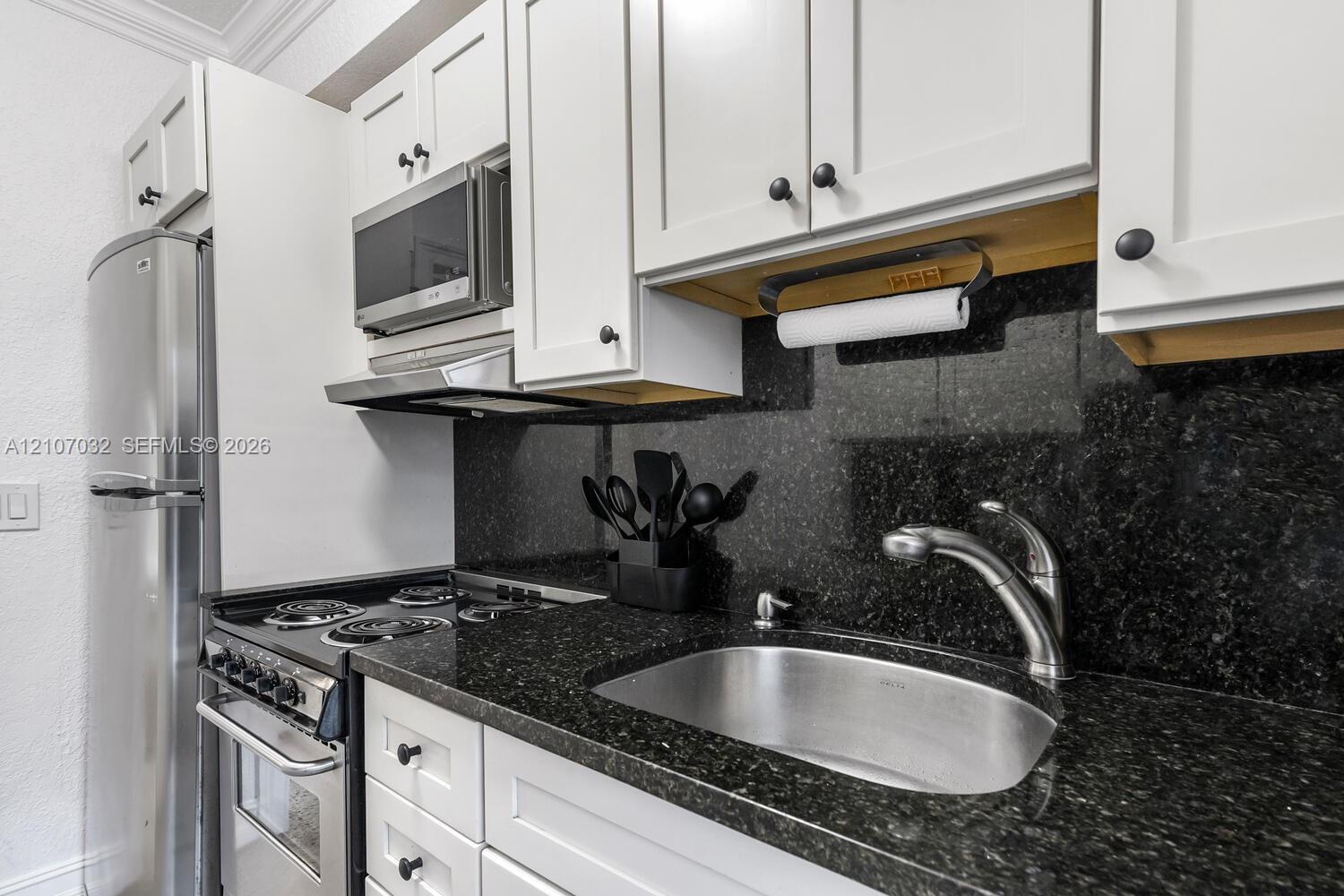 Kitchen featuring white shaker-style cabinetry, stone countertops, stainless steel appliances, and a deep-basin stainless steel sink with a high-arch faucet