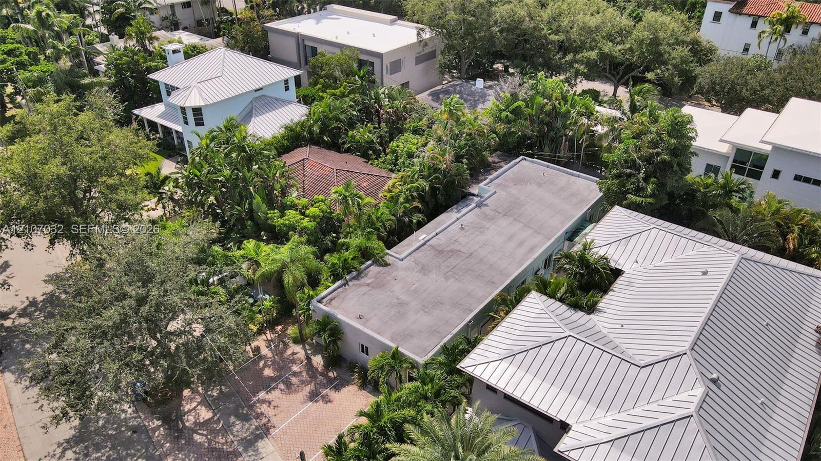 Aerial perspective of a multi-structure property featuring metal roof systems, paver driveway, and mature landscaping
