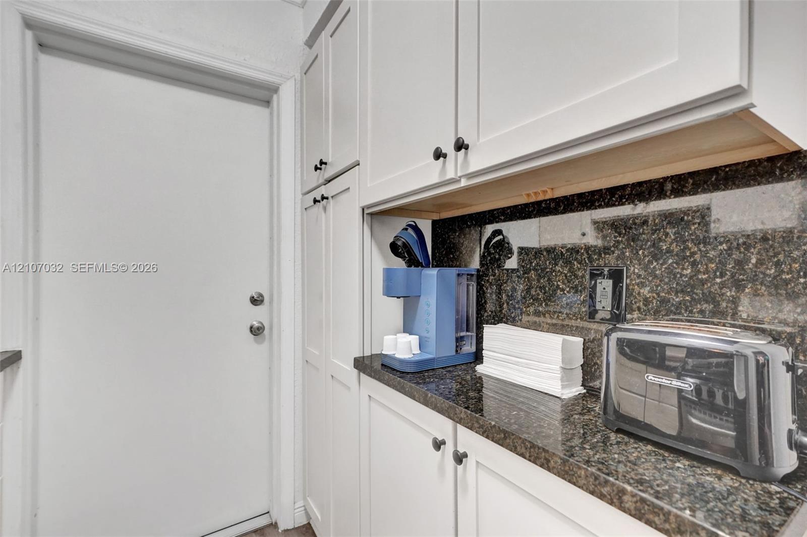White shaker-style cabinetry with dark stone countertops and a coordinating stone backsplash