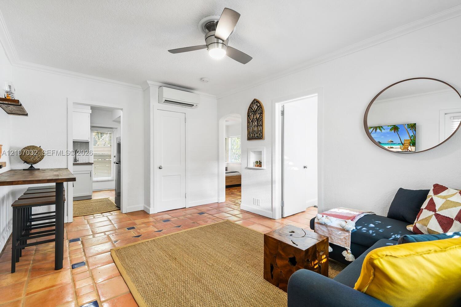 Terracotta tile flooring with inlaid decorative tiles, ceiling fan with integrated lighting, wall-mounted ductless air conditioning unit, and arched doorways