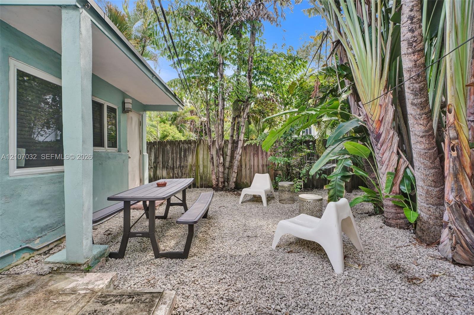 Exterior patio space featuring a gravel ground surface, privacy fencing, and established tropical vegetation