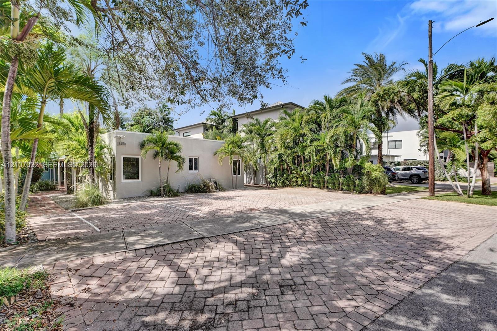 Exterior of the property featuring a paver driveway, light-toned stucco siding, and mature palm landscaping