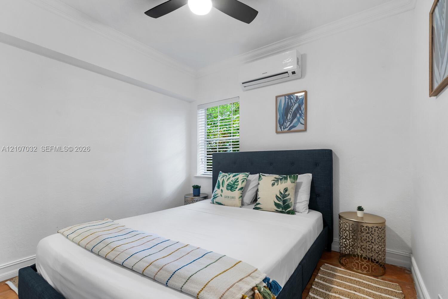 Interior space featuring wood-finish flooring, a wall-mounted ductless air conditioning unit, a multi-blade ceiling fan, and a window with white blinds