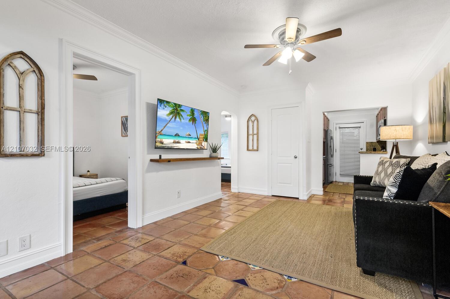 Interior space featuring terracotta tile flooring, crown molding, a ceiling fan with integrated lighting, and a wall-mounted wooden shelf