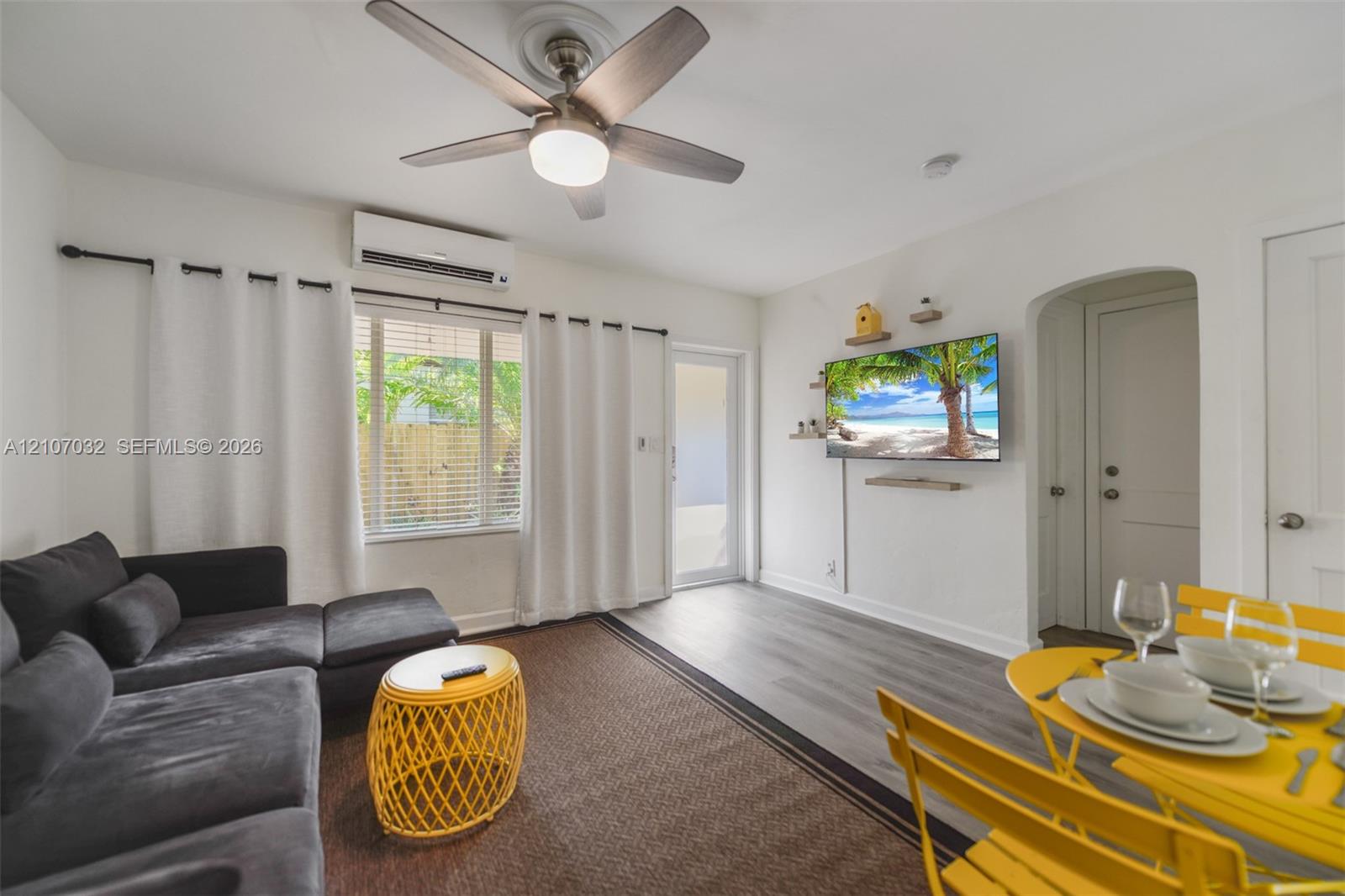 Neutral-toned wood-finish flooring, wall-mounted ductless mini-split HVAC unit, ceiling fan with integrated lighting, and an arched doorway