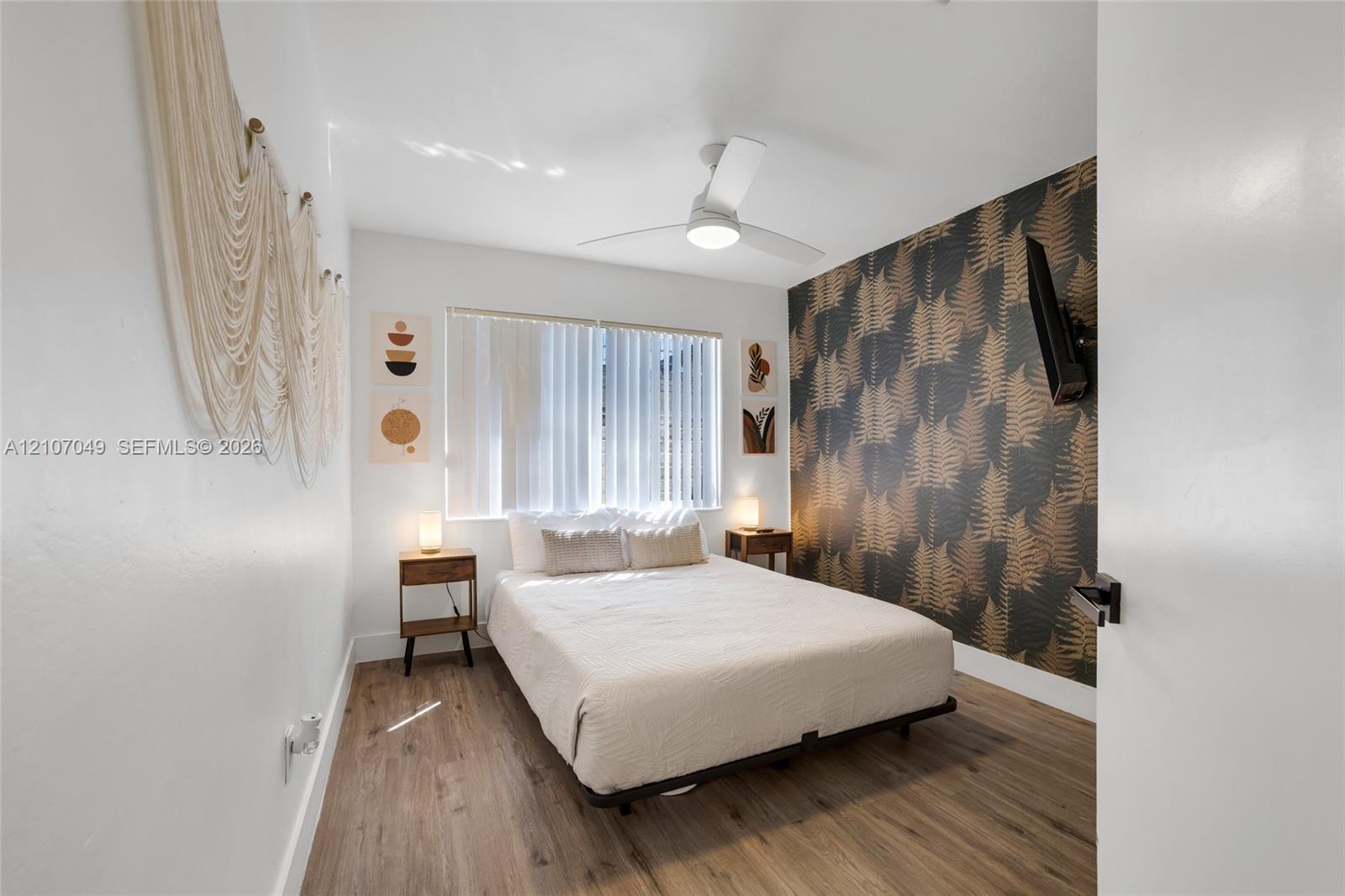 Wood-finish flooring, patterned accent wall, and ceiling fan with integrated lighting