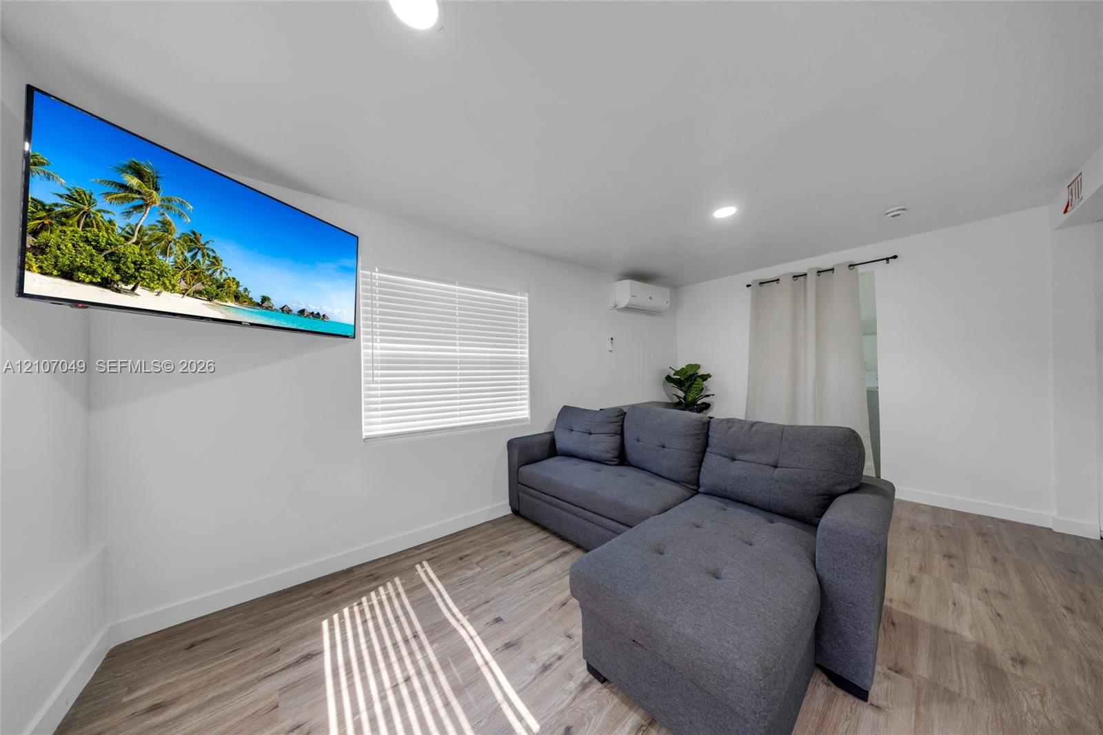 Room featuring wood-finish flooring, recessed lighting, wall-mounted ductless heating and cooling unit, and horizontal window blinds