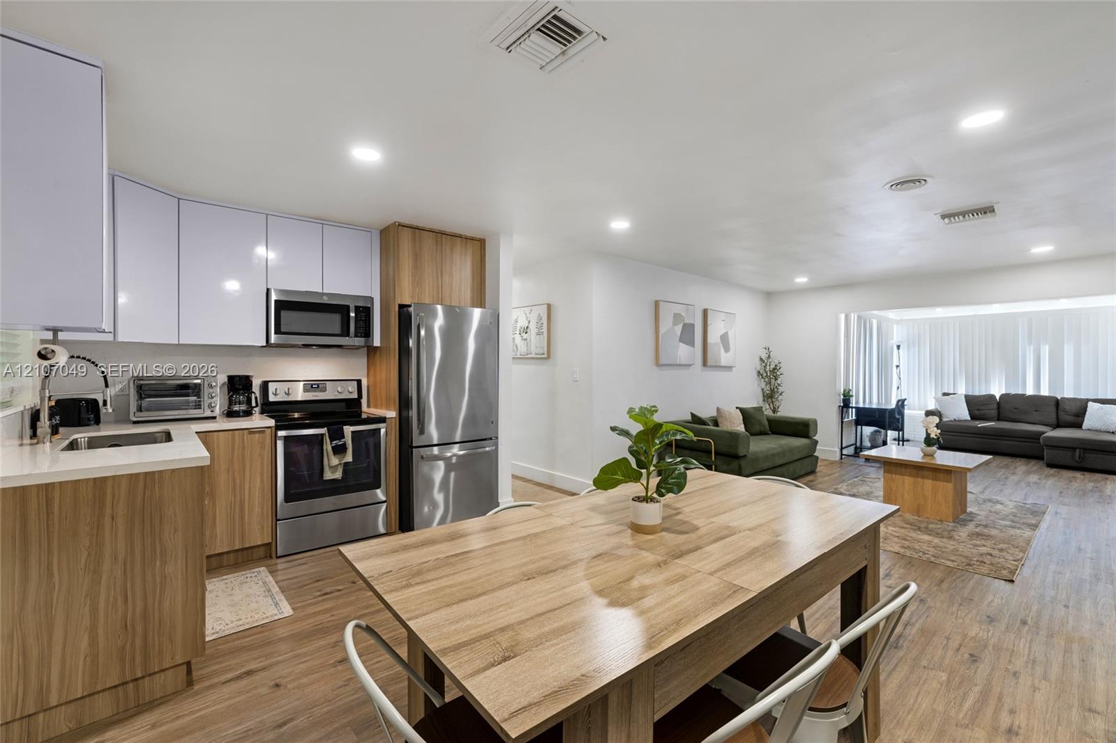 Kitchen featuring wood-finish cabinetry, white upper cabinets, stainless steel appliances, and wood-finish flooring