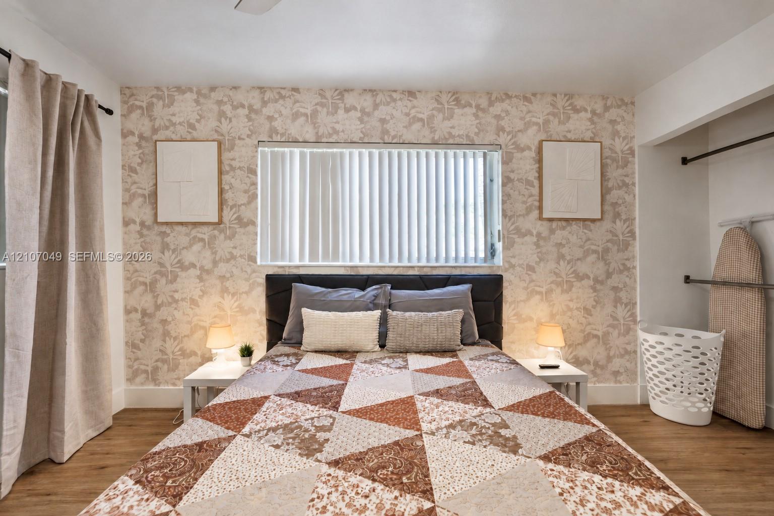 Neutral-toned patterned wallpaper, wood-finish flooring, horizontal window blinds, and recessed closet space with built-in metal rods