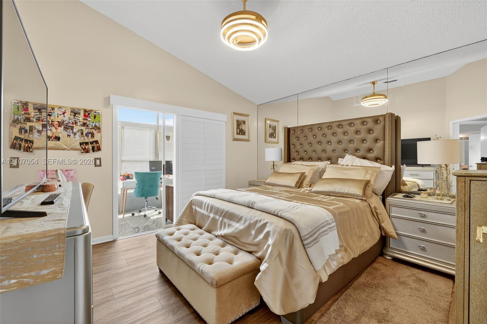 Vaulted ceilings, laminate flooring, full-wall mirrored accent, tiered pendant lighting, and sliding glass door leading to the Florida Room