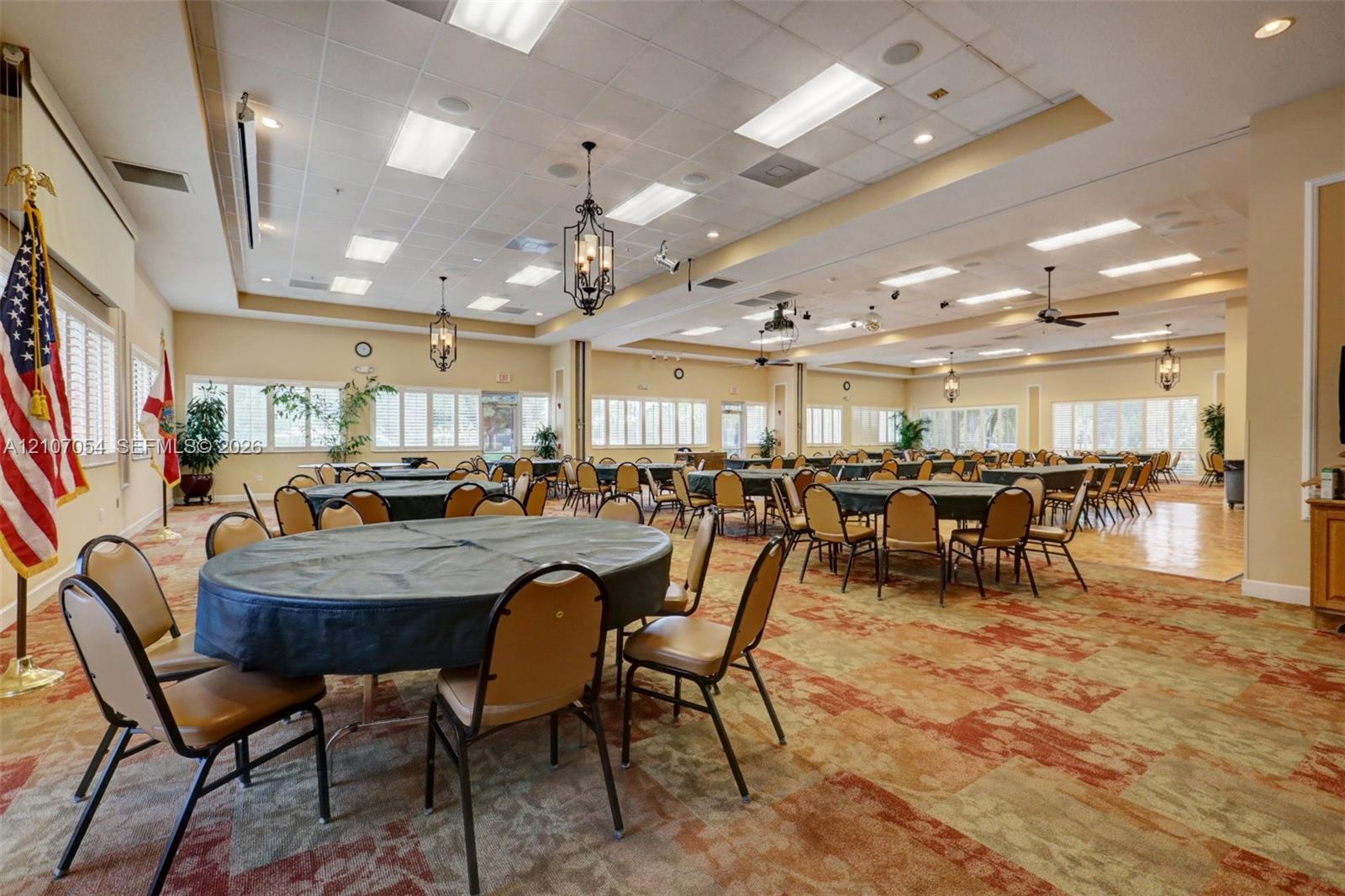 Clubhouse featuring expansive event space featuring a recessed drop-ceiling with inset lighting, multiple decorative hanging lanterns, wall-to-wall patterned carpeting, and a perimeter of horizontal window blinds