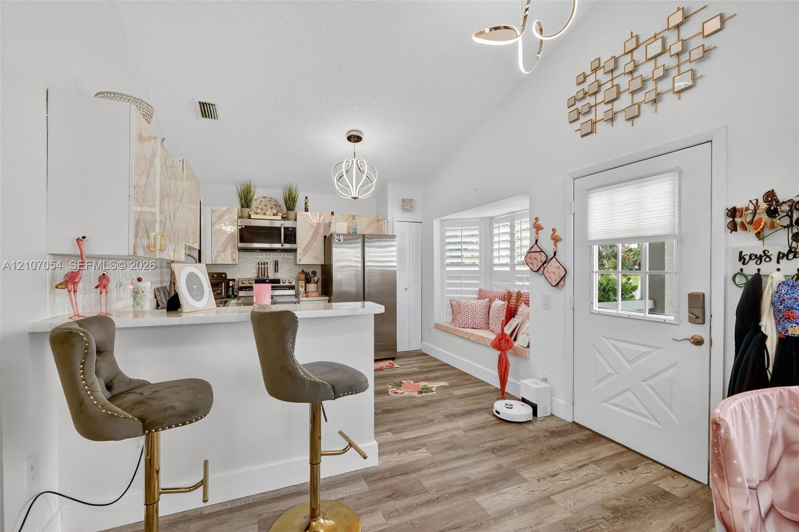 Vaulted ceilings, laminate flooring, kitchen peninsula with counter seating, built-in window seat, and modern geometric light fixtures