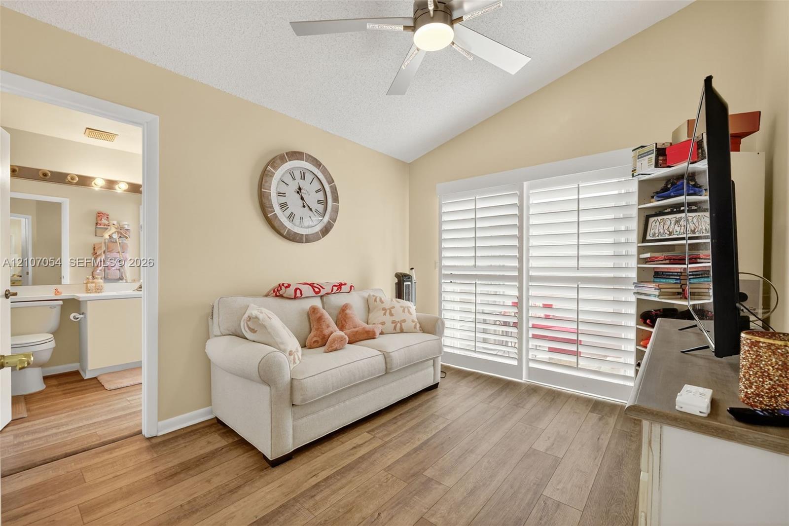 Vaulted ceiling with a centrally mounted ceiling fan, laminate flooring, and white plantation shutters