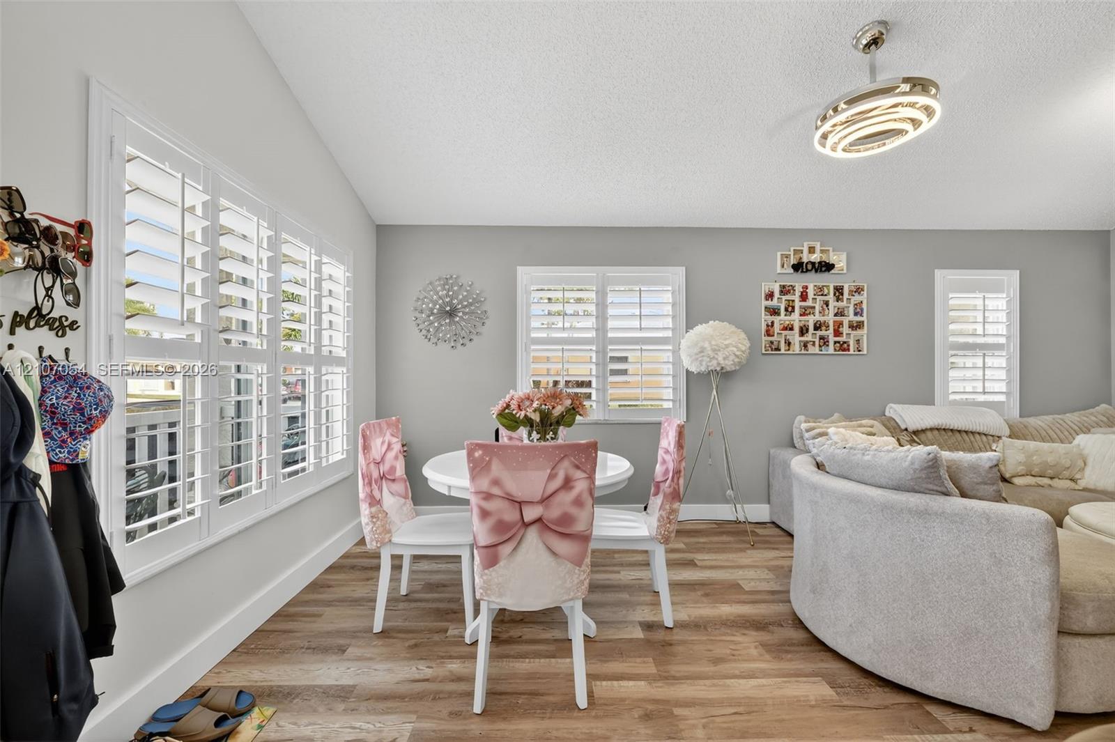 Vaulted ceilings, laminate flooring, white plantation shutters, and a modern circular chandelier