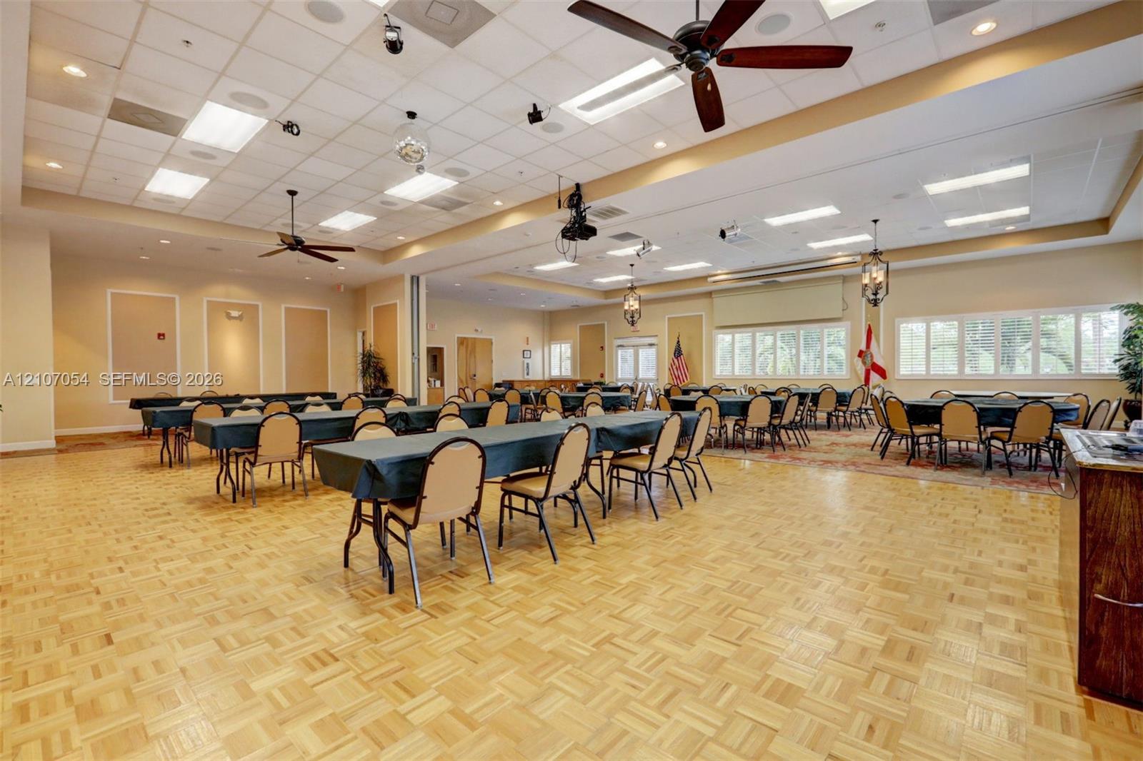 Clubhouse featuring expansive hall featuring parquet wood-finish flooring, a coffered ceiling with recessed lighting, multiple ceiling fans, and large paneled windows