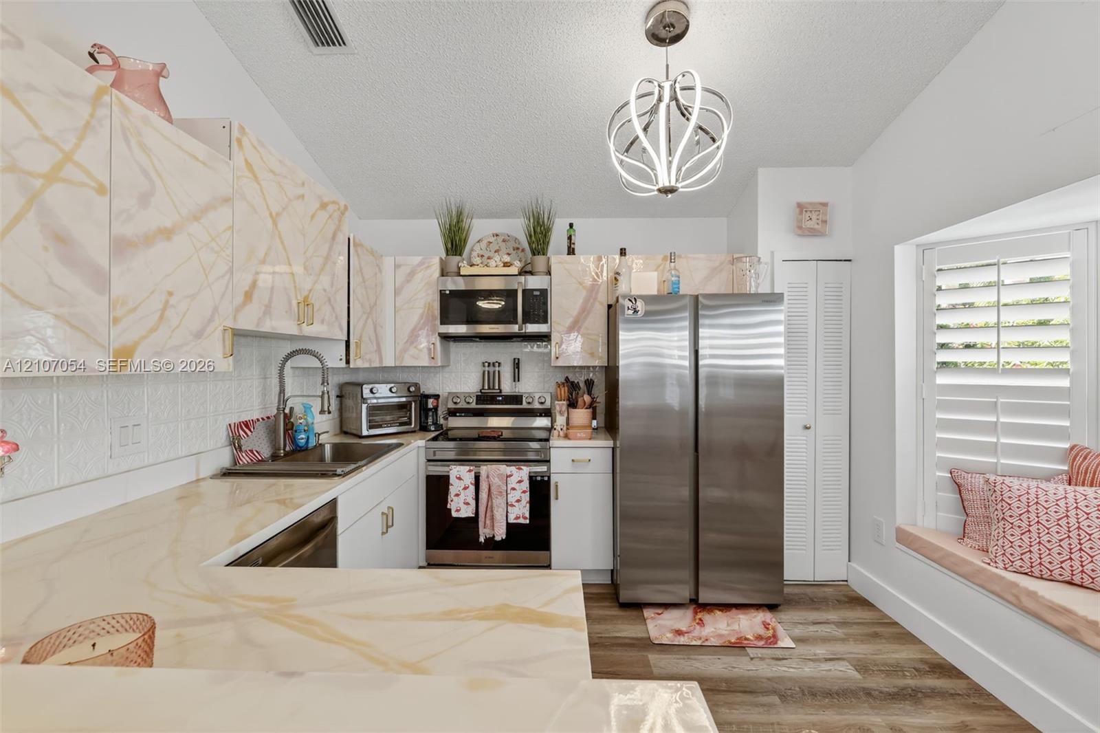 Kitchen featuring patterned cabinetry, granite countertops, stainless steel appliances, laminate flooring, and a built-in window seat with plantation shutters