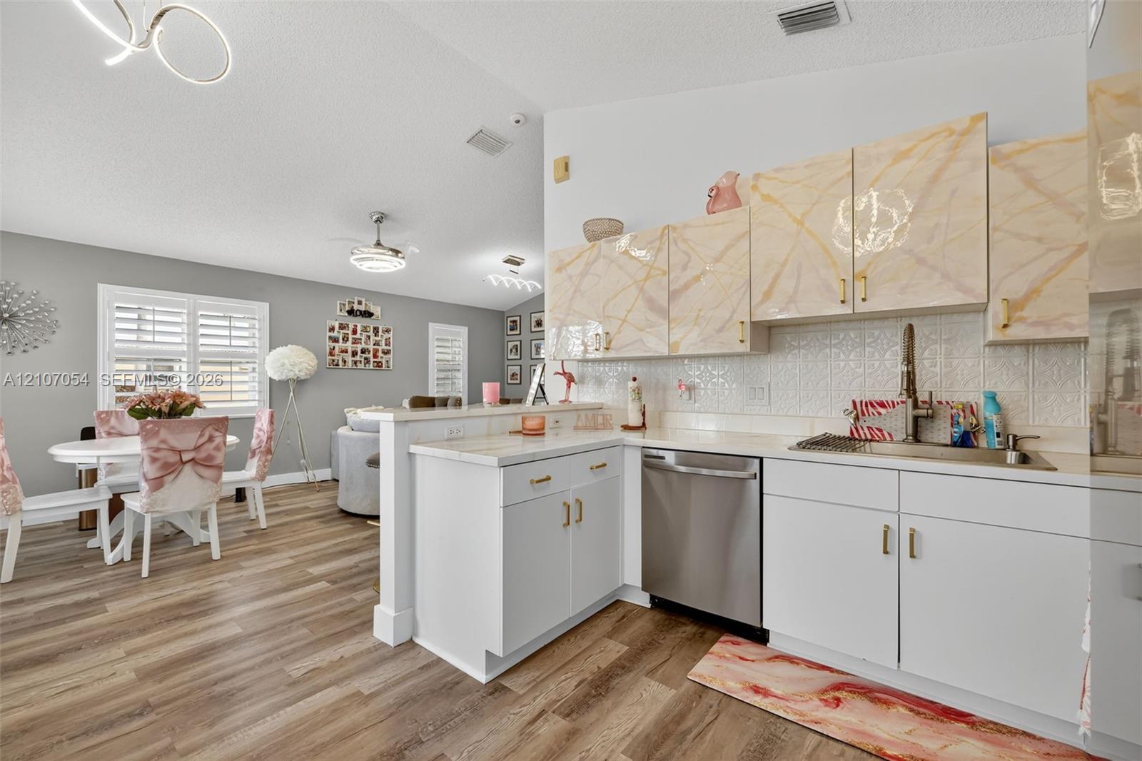 Kitchen featuring white lower cabinetry, patterned upper cabinetry, stainless steel dishwasher, light-toned granite countertop, and laminate flooring