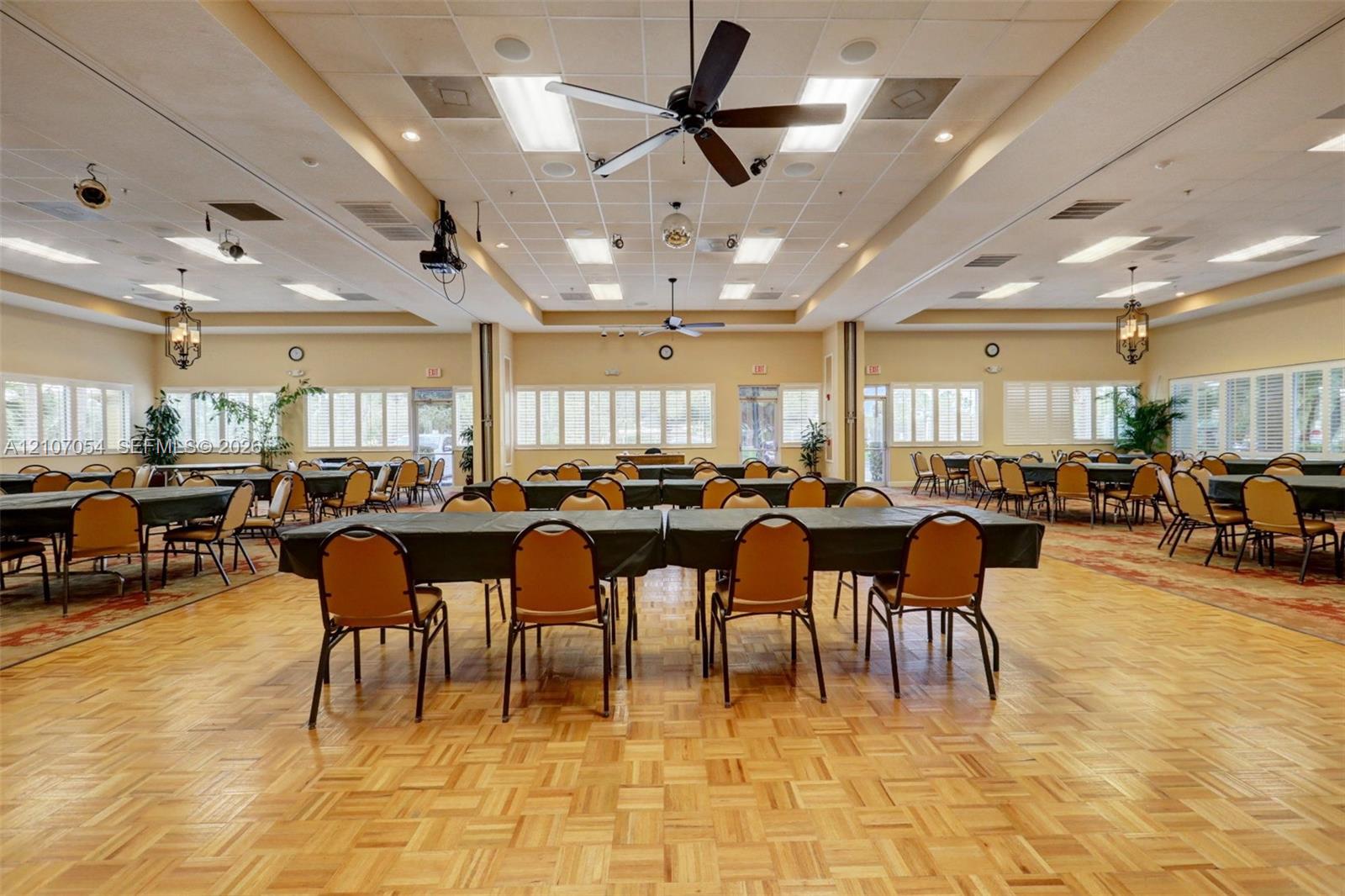 Clubhouse featuring expansive multipurpose room featuring parquet wood flooring, recessed tray ceiling, multiple inset ceiling fans, and a wide array of windows along the perimeter