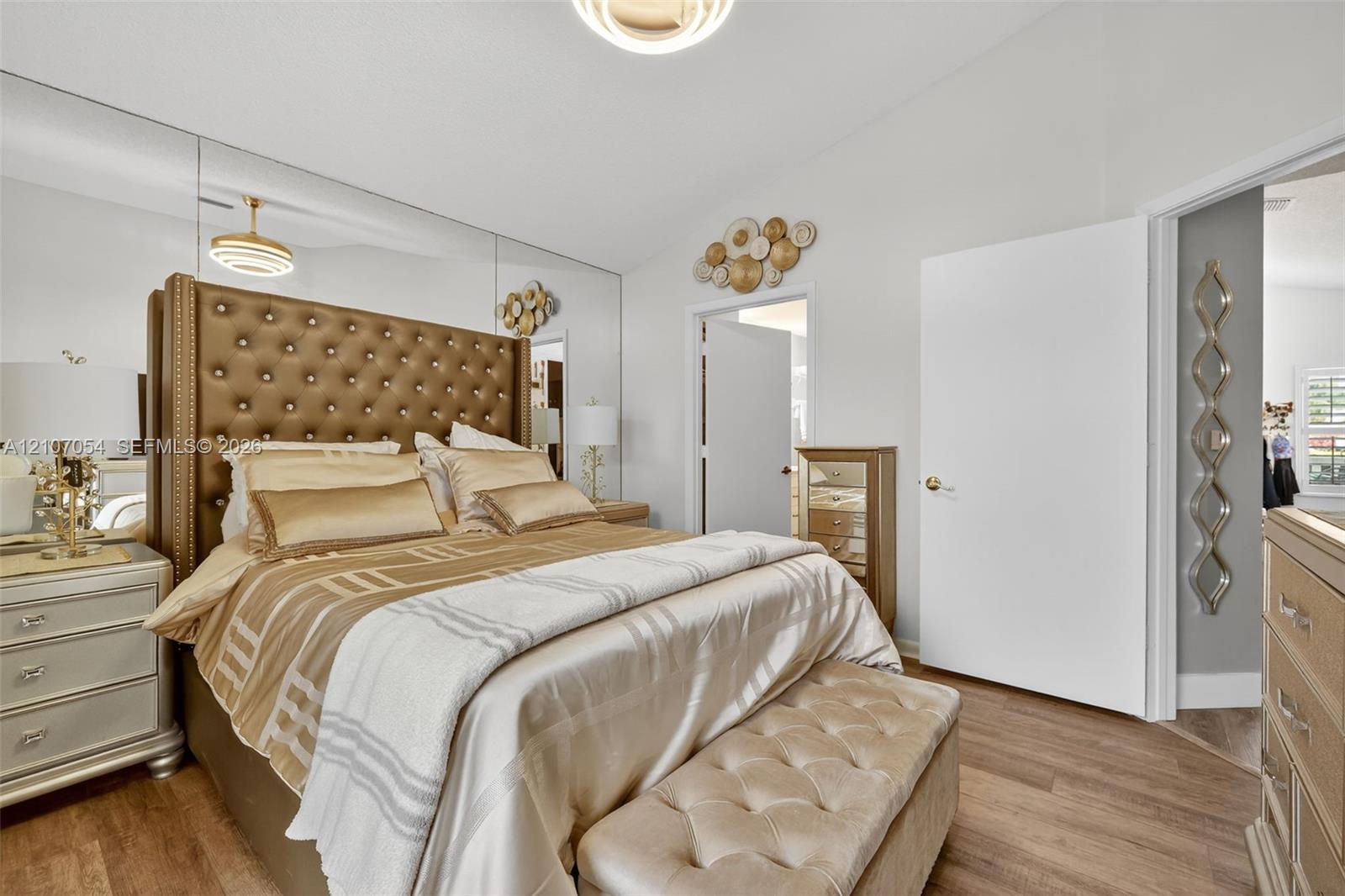 Vaulted ceilings featuring a circular flush-mount light fixture, full-wall mirrored accent, and laminate flooring
