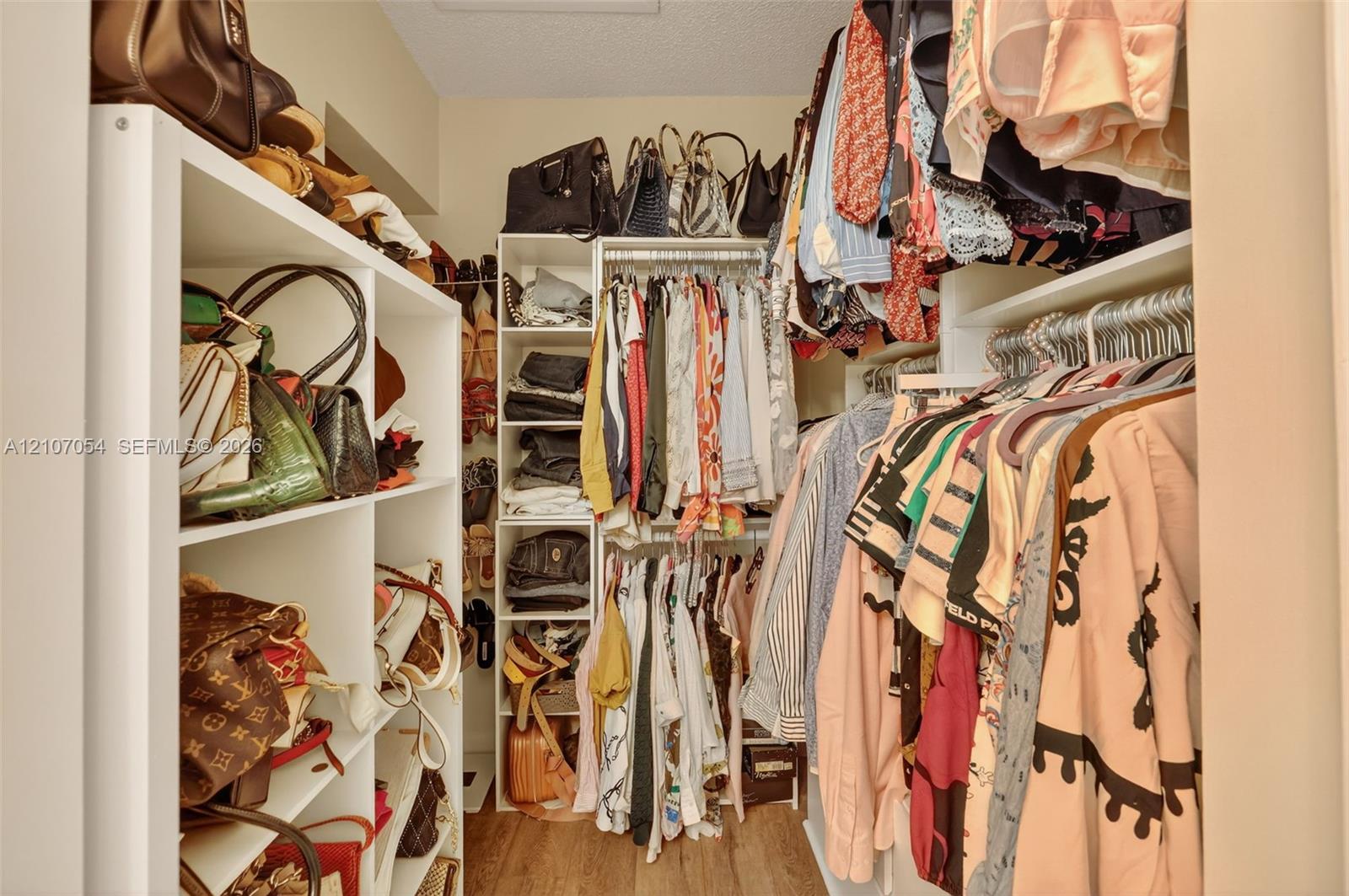 Primary bedroom walk-in closet featuring white built-in shelving, vertical storage compartments, and hanging rods