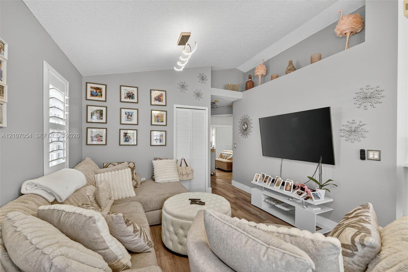 Vaulted ceiling featuring a modern geometric light fixture, laminate flooring and plantation shutters