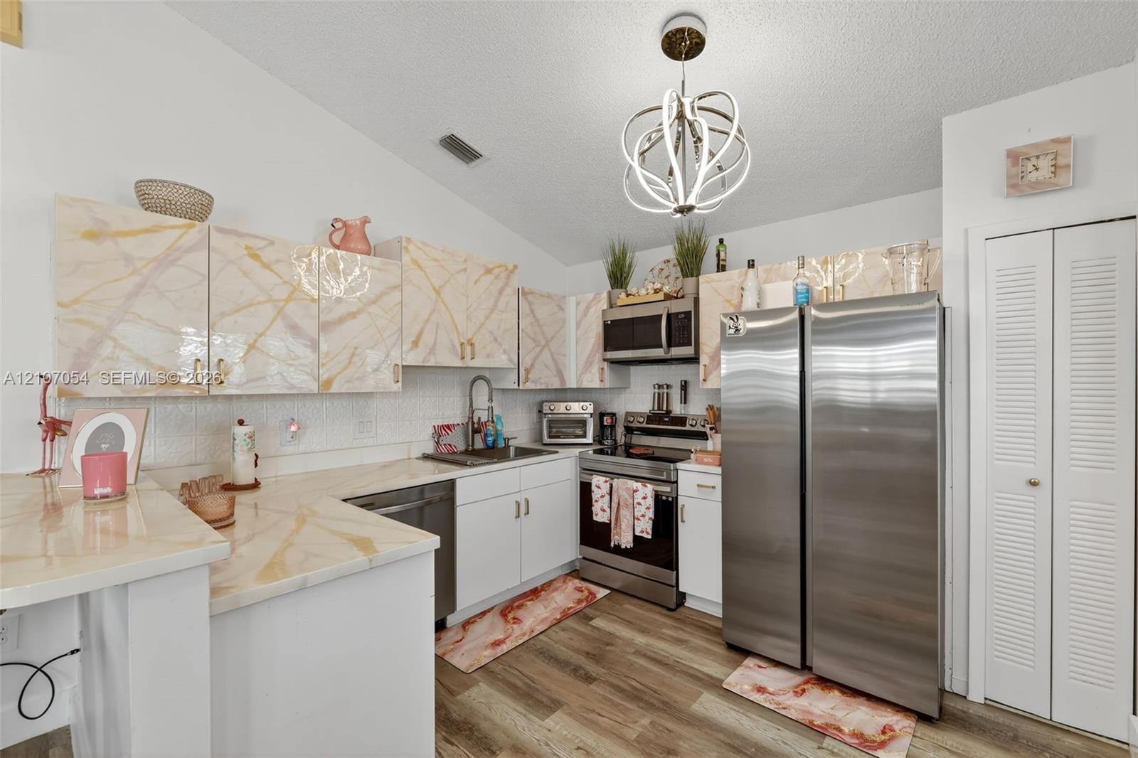 Kitchen featuring stone-finish cabinetry, laminate flooring, stainless steel appliances, and a modern sculptural pendant light