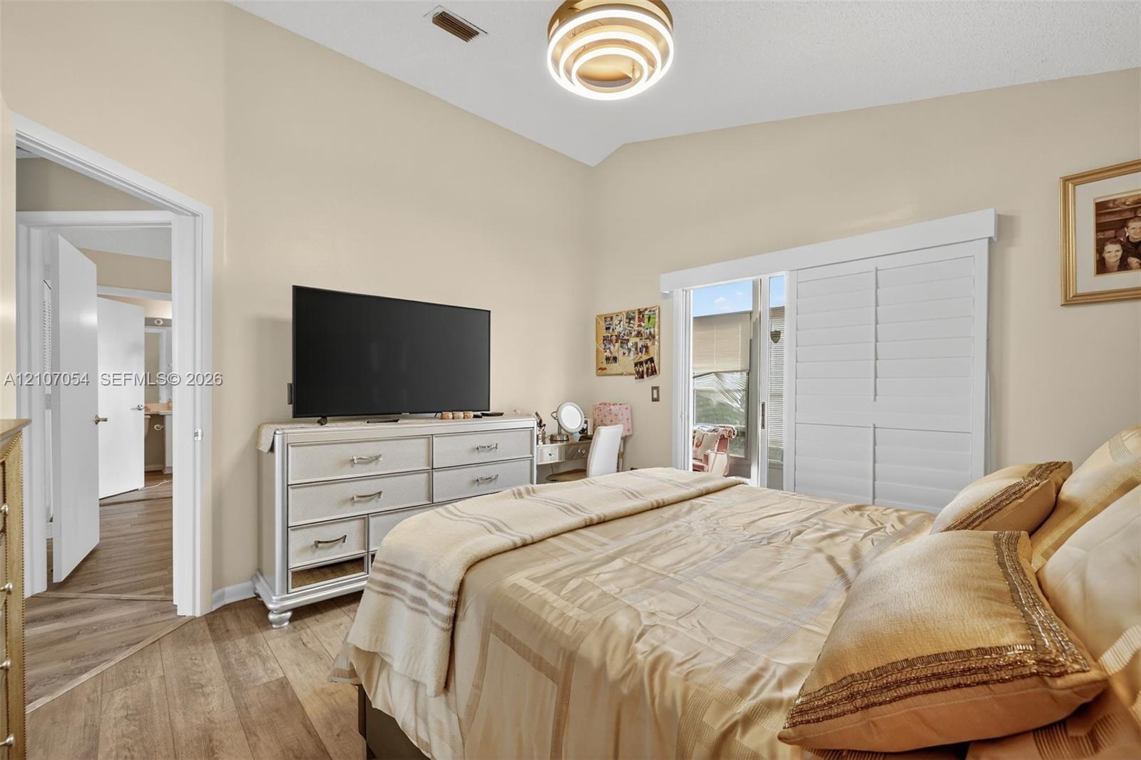 Vaulted ceiling featuring a modern multi-ring pendant light, sliding glass door with plantation shutters leading to the Florida Room, and laminate flooring