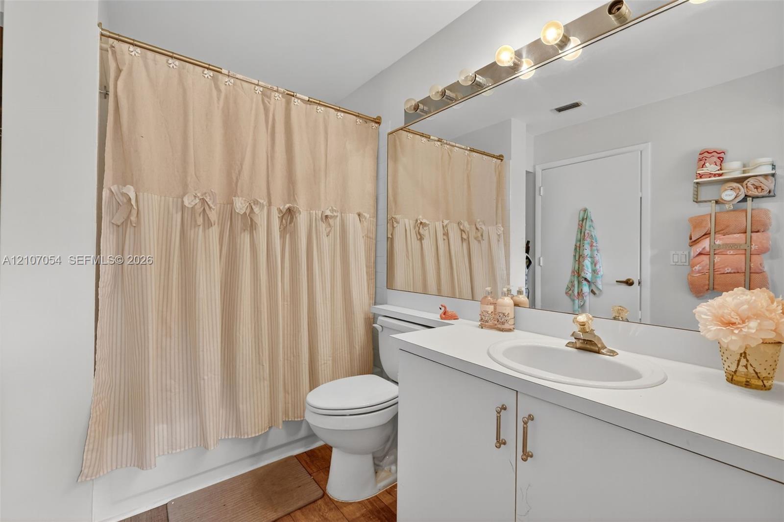 Bathroom featuring a white vanity cabinet with an oval undermount sink, solid surface countertop, metallic faucet, large wall-mounted mirror, and multi-bulb strip lighting