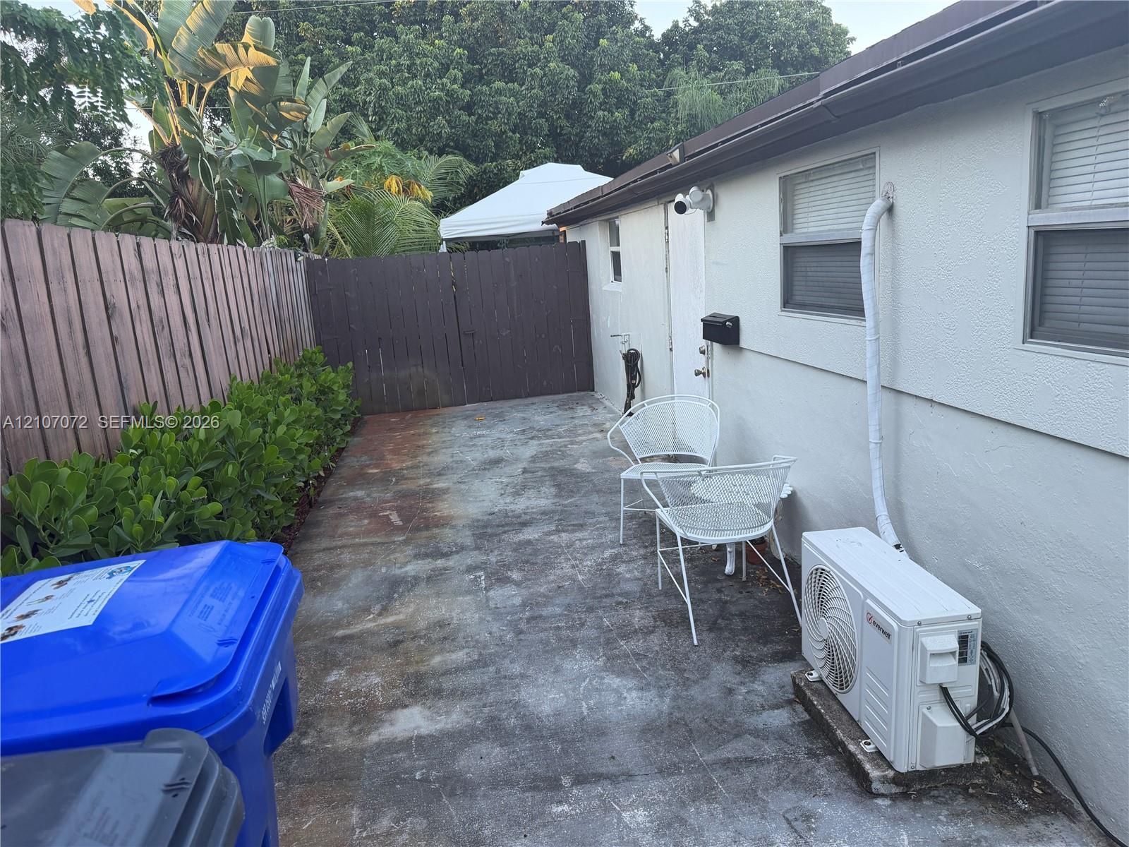 Concrete patio area enclosed by wood fencing and perimeter hedge screening