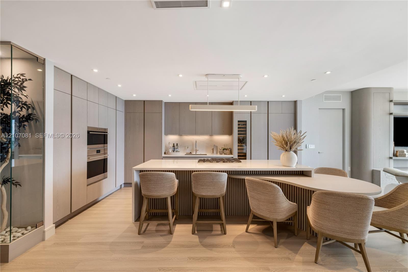 Modern kitchen featuring floor-to-ceiling cabinetry, a central island with integrated seating, built-in stainless steel appliances, wood-finish flooring, and recessed lighting