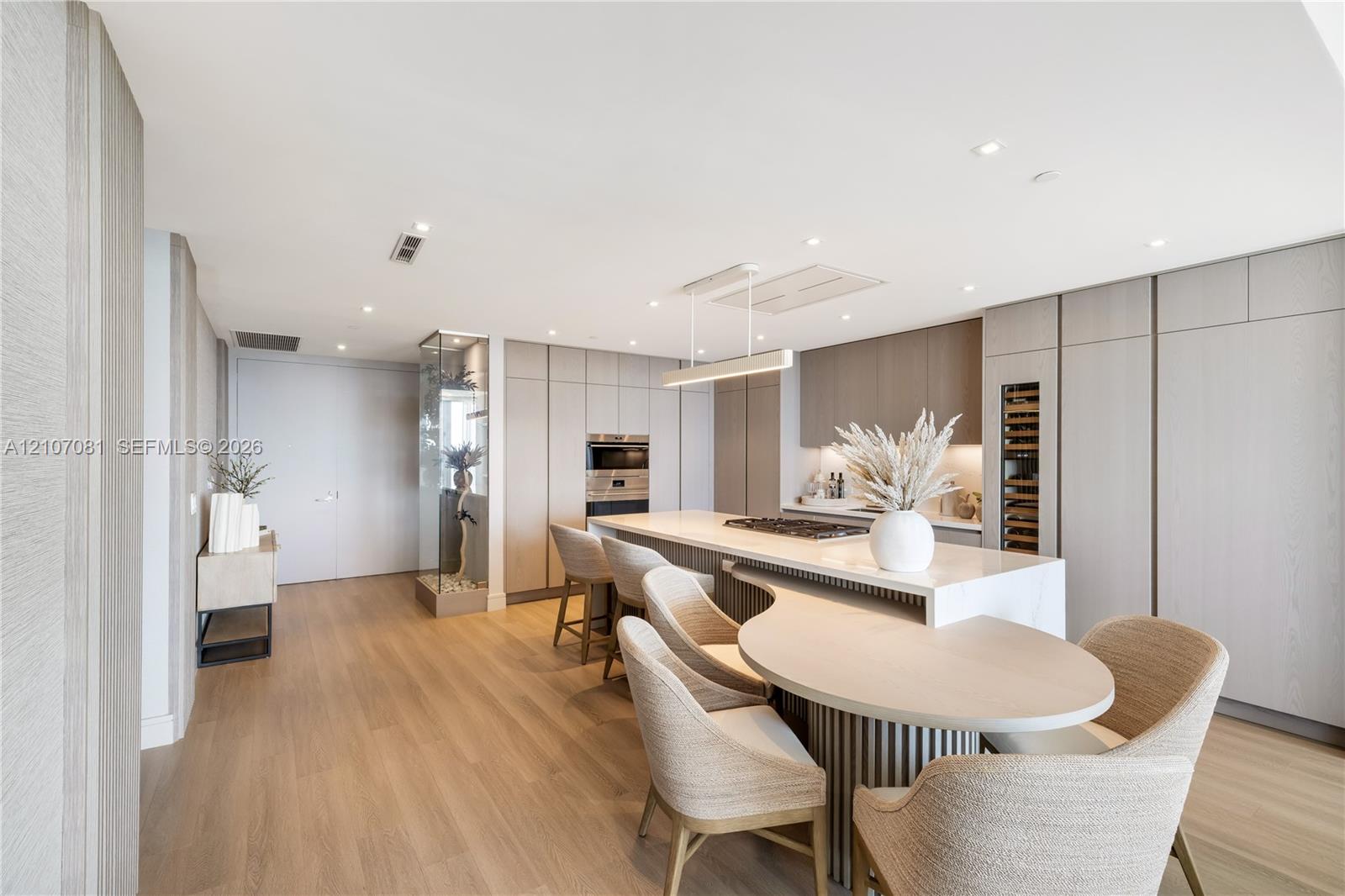 Kitchen featuring floor-to-ceiling cabinetry, a central stone-top island with an integrated gas cooktop, a built-in wine refrigerator, wood-finish flooring, and recessed lighting