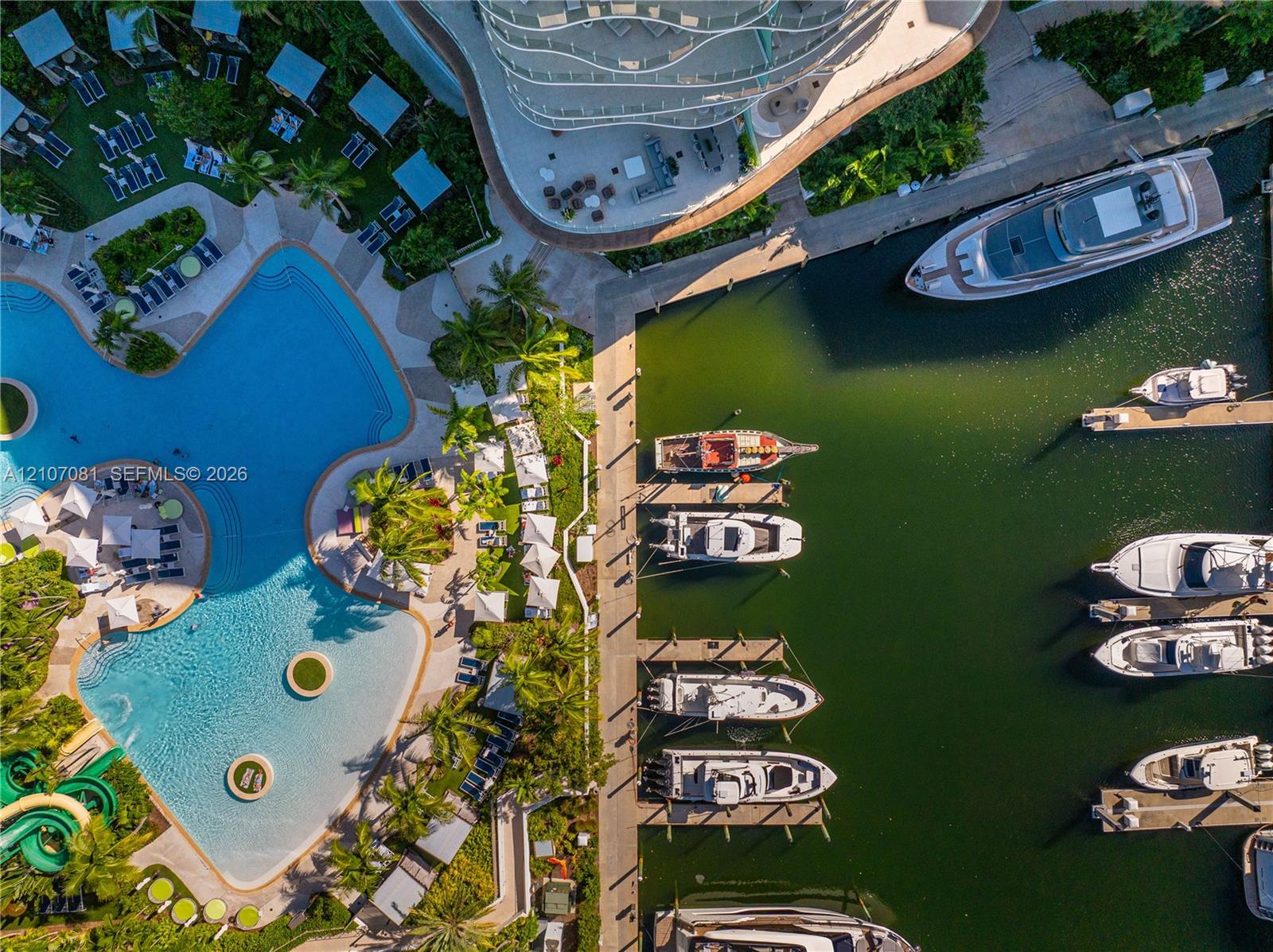Aerial perspective of a multi-vessel deep-water marina featuring fixed concrete dockage and a large-scale swimming pool with integrated water slide and palm-landscaped deck