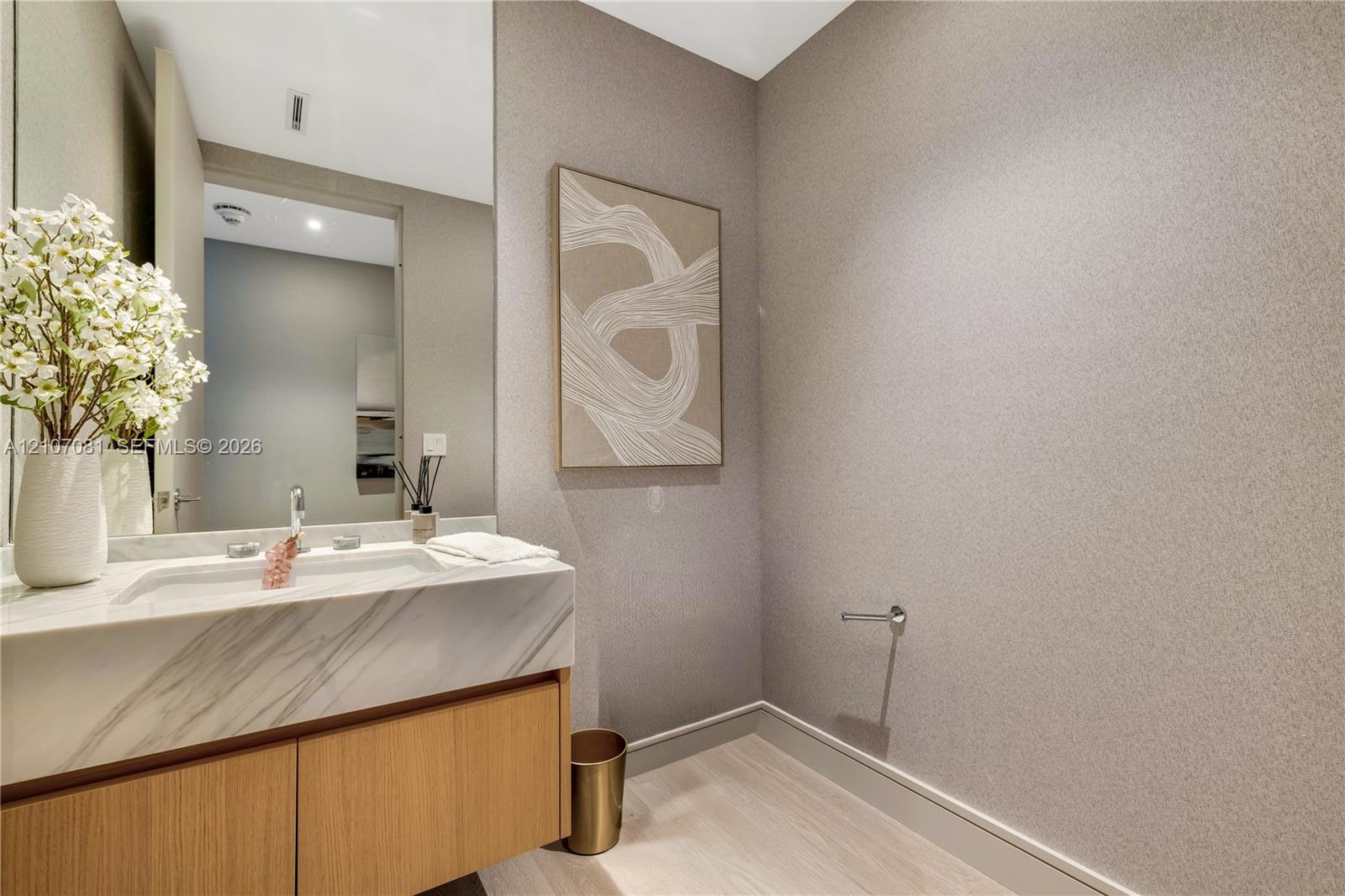 Floating vanity with light wood-finish cabinetry, stone countertop featuring integrated sink, polished metal faucet, and textured wall finish