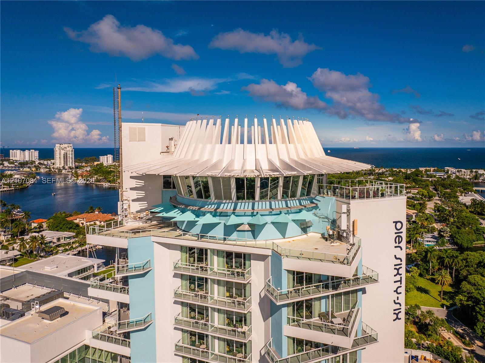 High-rise building featuring a distinctively sculpted crown, expansive floor-to-ceiling glass windows, tiered private balconies, and a reinforced concrete exterior
