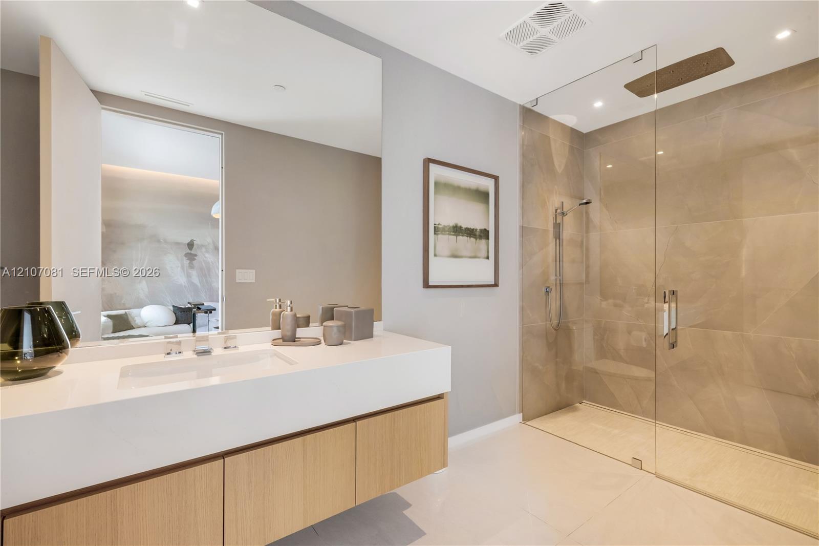 Floating vanity with integrated sink and stone-composite countertop, large-format tiled walk-in shower with frameless glass enclosure, ceiling-mounted rainfall showerhead, and expansive wall-to-wall mirror