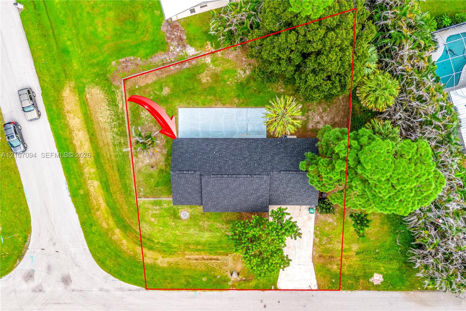 Aerial perspective of a property lot featuring mature landscaping, a paved driveway, and an expansive lawn