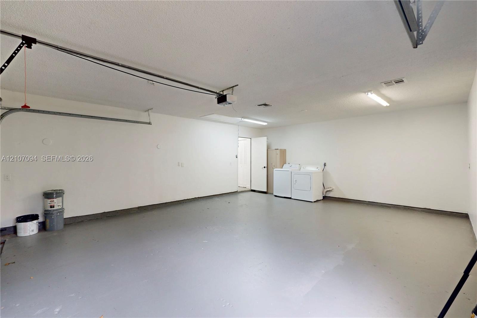 Two-car garage featuring a painted concrete floor, textured ceiling, fluorescent lighting, and dedicated laundry hookups