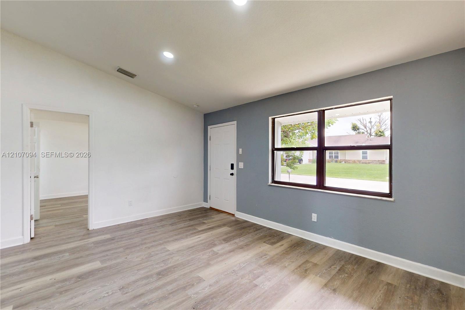 Vaulted ceilings, wood-finish flooring, recessed lighting, and a large picture window with dark-toned frames