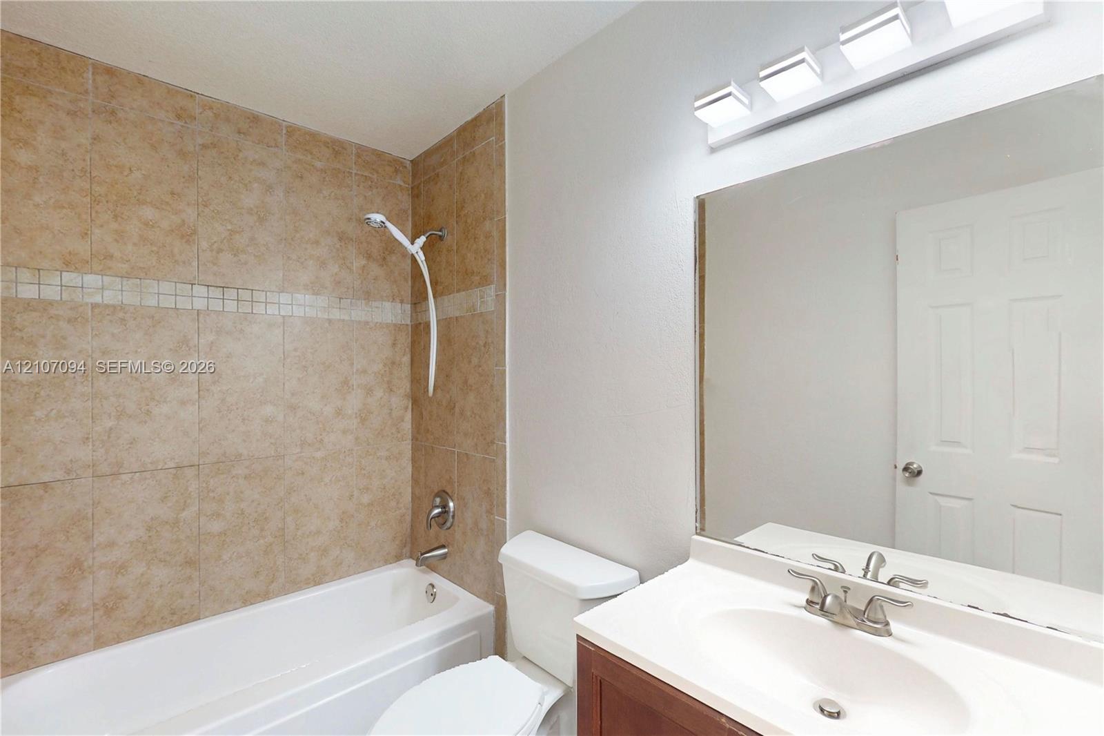Bathroom featuring a tiled tub surround with decorative accent inlay, a vanity with an integrated basin, a large wall-mounted mirror, and a four-light fixture