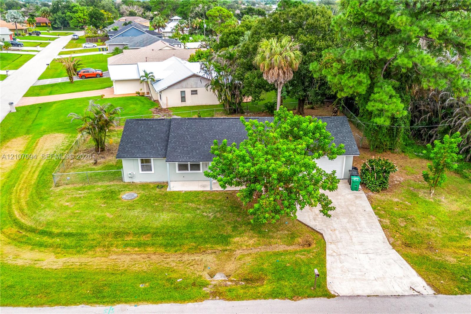 Single-story residence featuring a shingle roof, concrete driveway, and expansive lawn with mature trees