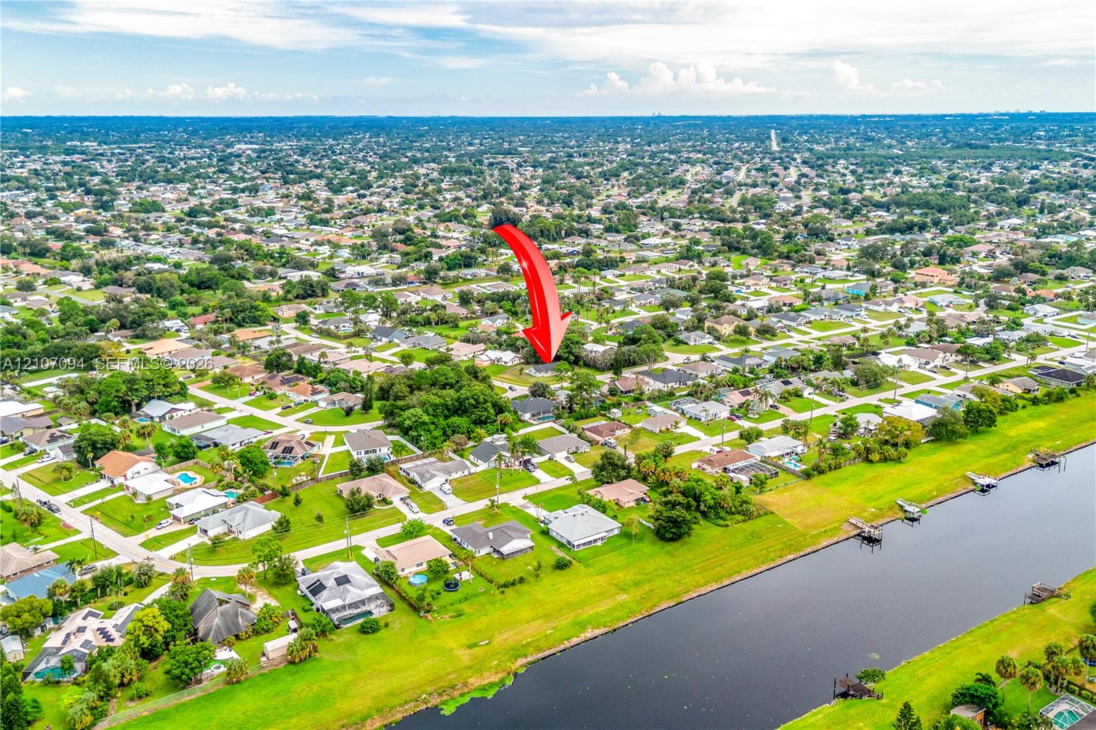 Aerial view of the residential property featuring mature trees, a multi-pitched roofline, and access to a canal
