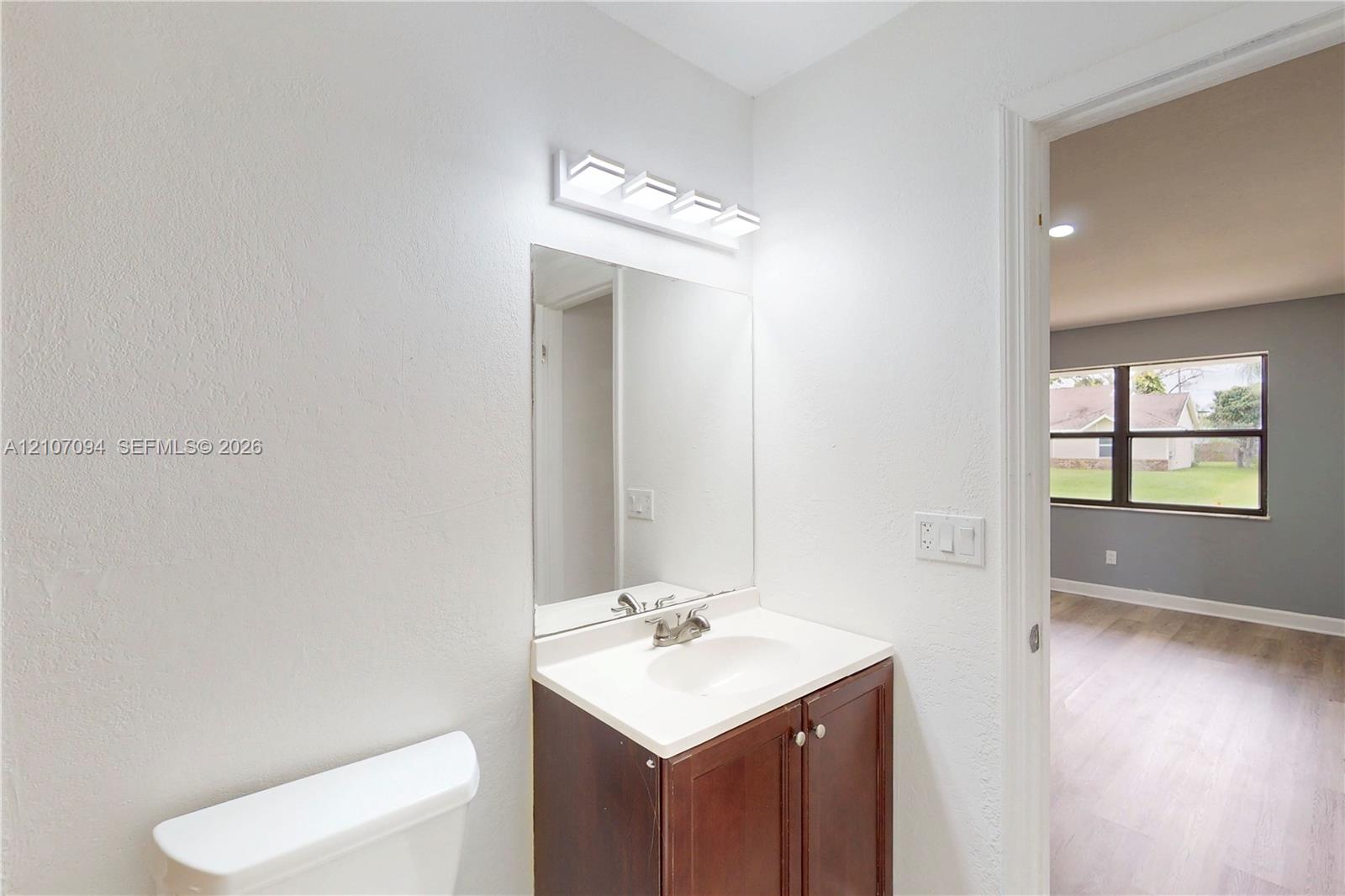 Bathroom featuring a dark wood-finish vanity with a white countertop, integrated basin, four-light vanity fixture, and frameless mirror