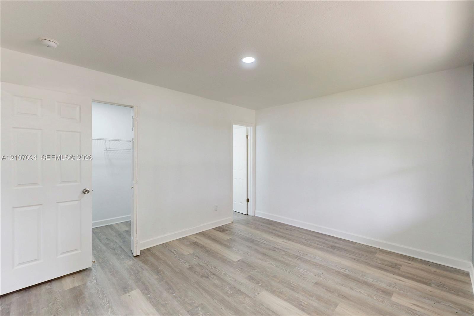 Room featuring wood-finish flooring, recessed lighting, and a six-panel door leading to a walk-in closet with built-in shelving