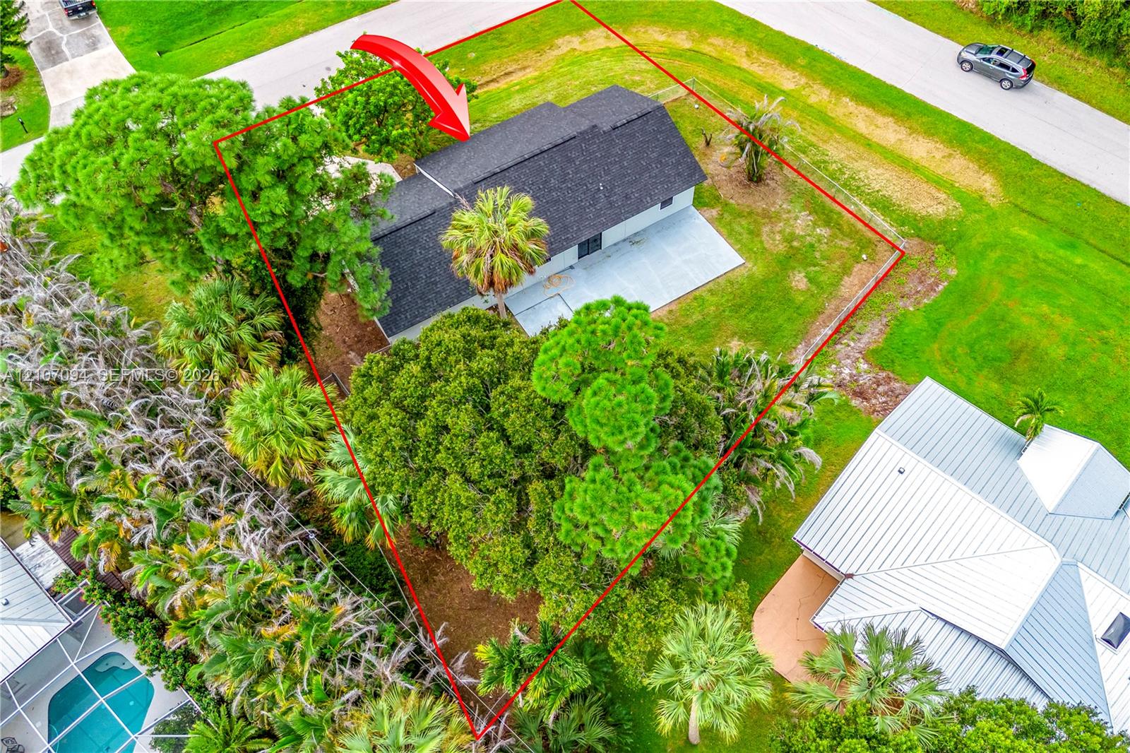 Aerial view of property featuring a shingle roof, concrete patio, expansive lawn, and mature canopy trees