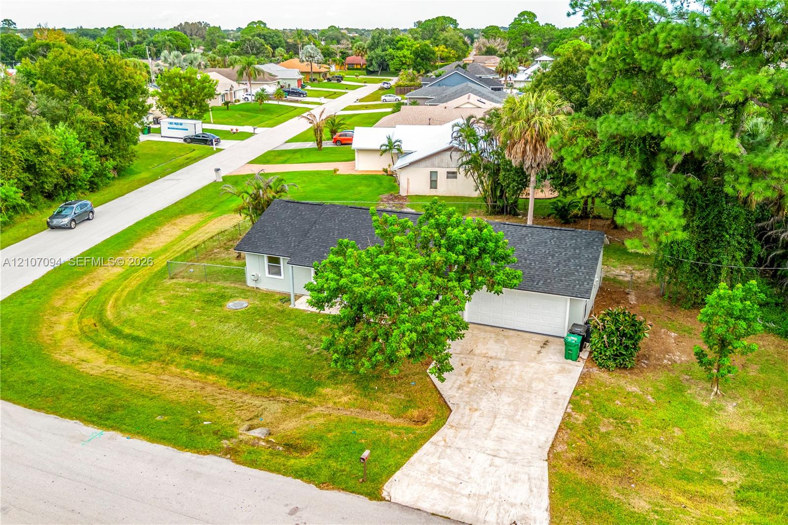 Single-story residence featuring a shingled roof, attached two-car garage, concrete driveway, and established landscaping on a corner lot