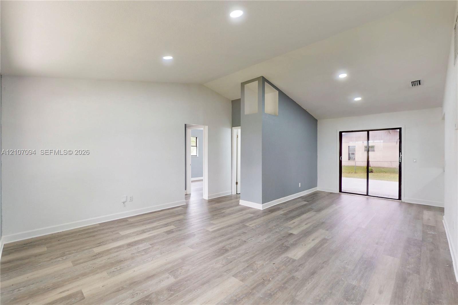 Vaulted ceilings, wood-finish flooring, recessed lighting, accent wall, and sliding glass doors